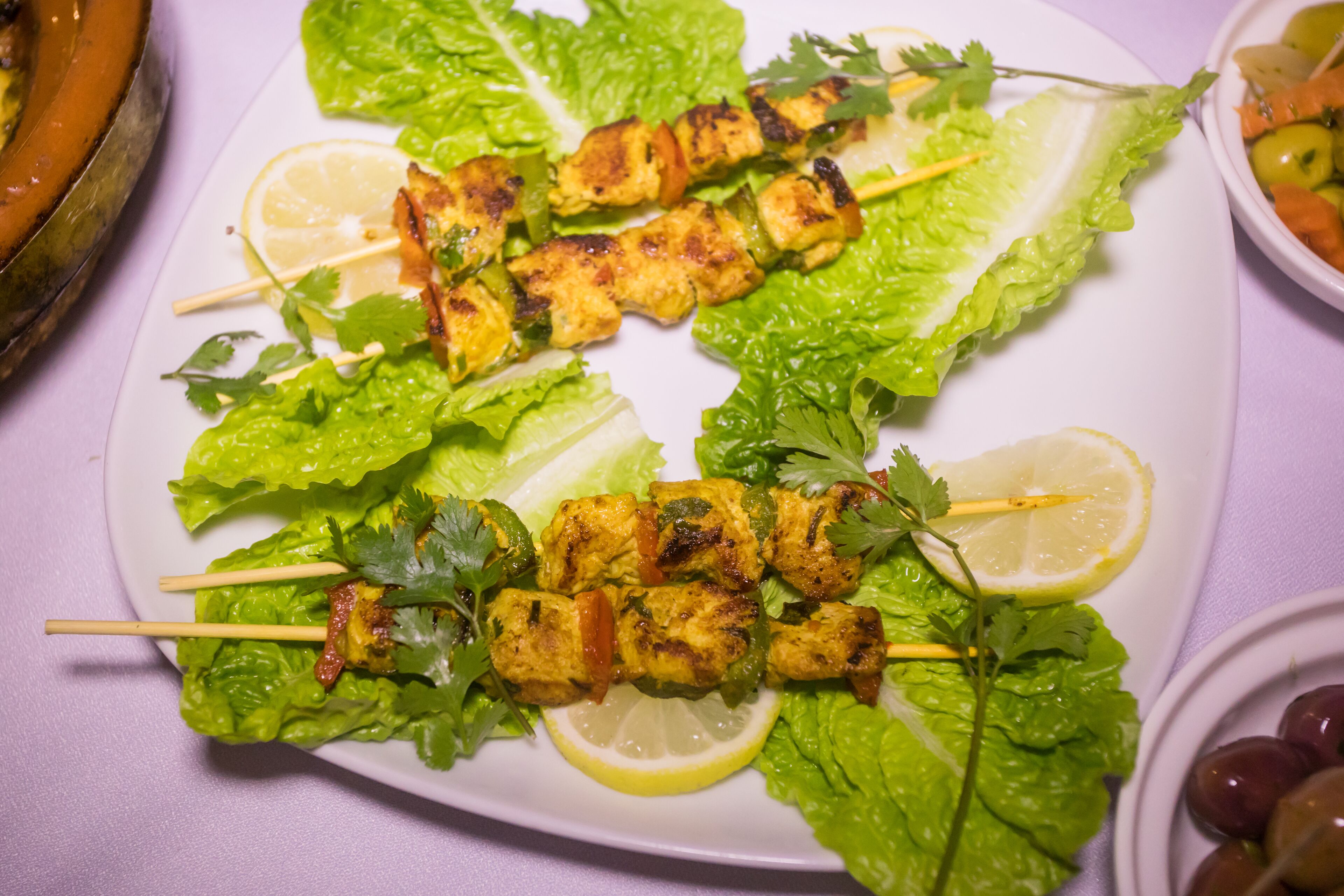 A plate of grilled chicken skewers with lettuce and lemon slices.