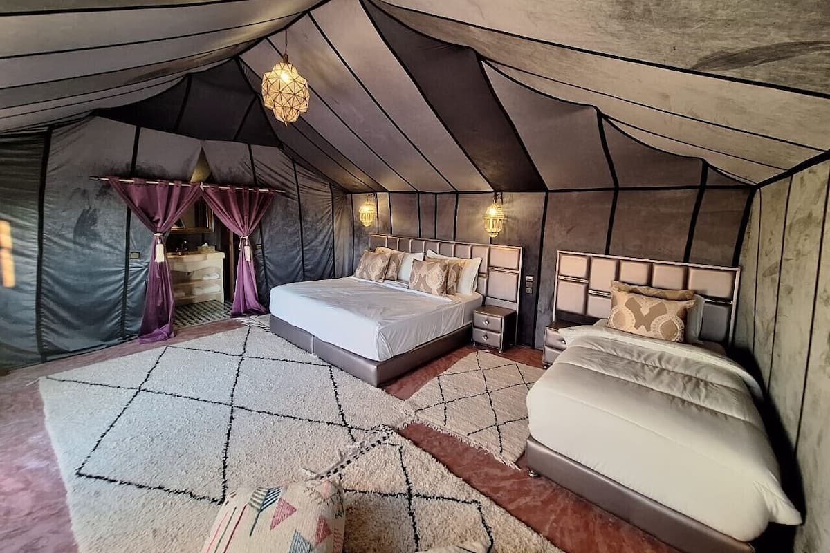 Quarto tipo tenda com duas camas, um tapete grande e um candeeiro pendente.