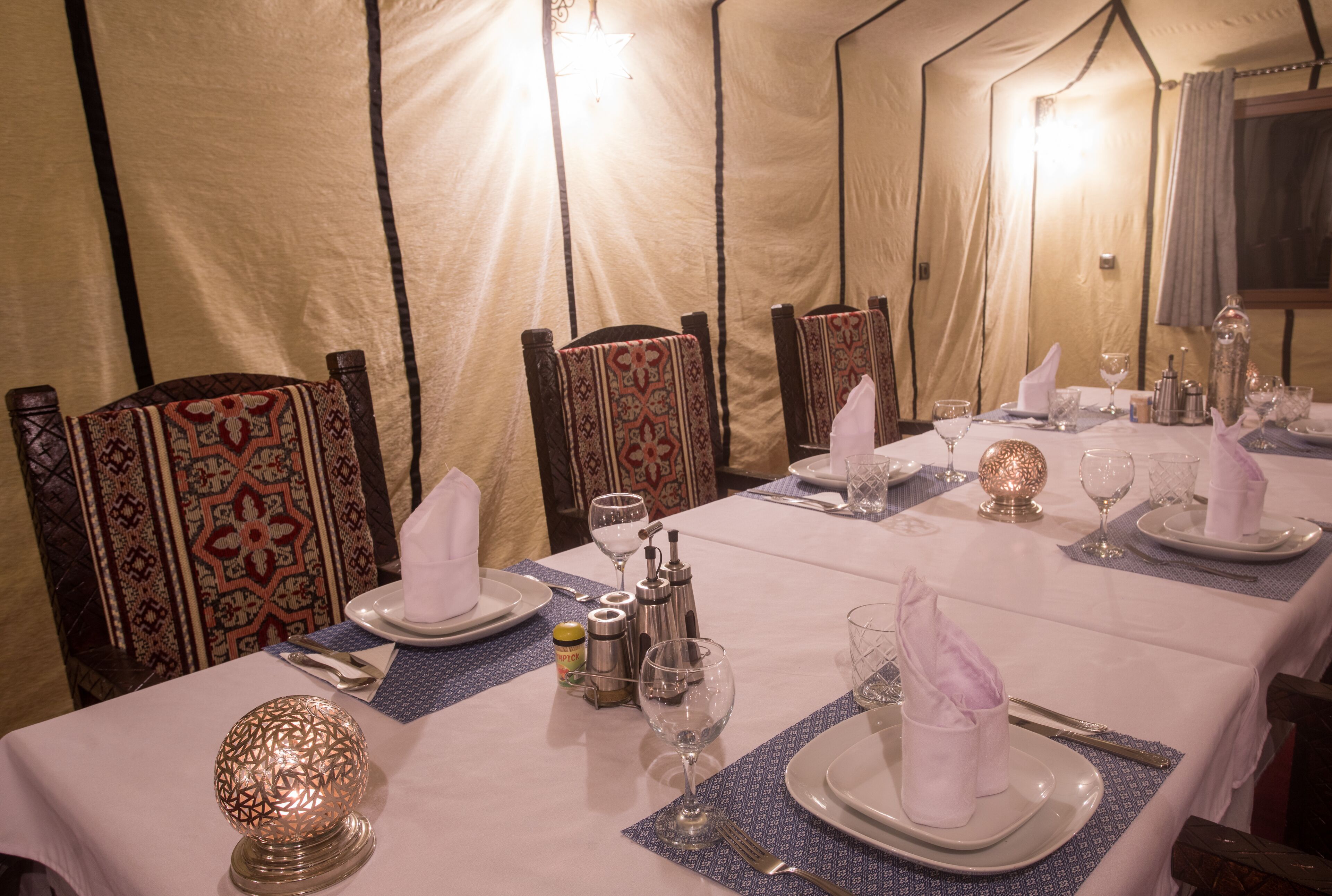A tented dining area with tables set for four, each with white tablecloths, silverware, and glassware.