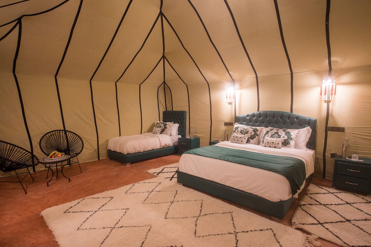 Um quarto tipo tenda com duas camas, uma mesinha com frutas e duas cadeiras.