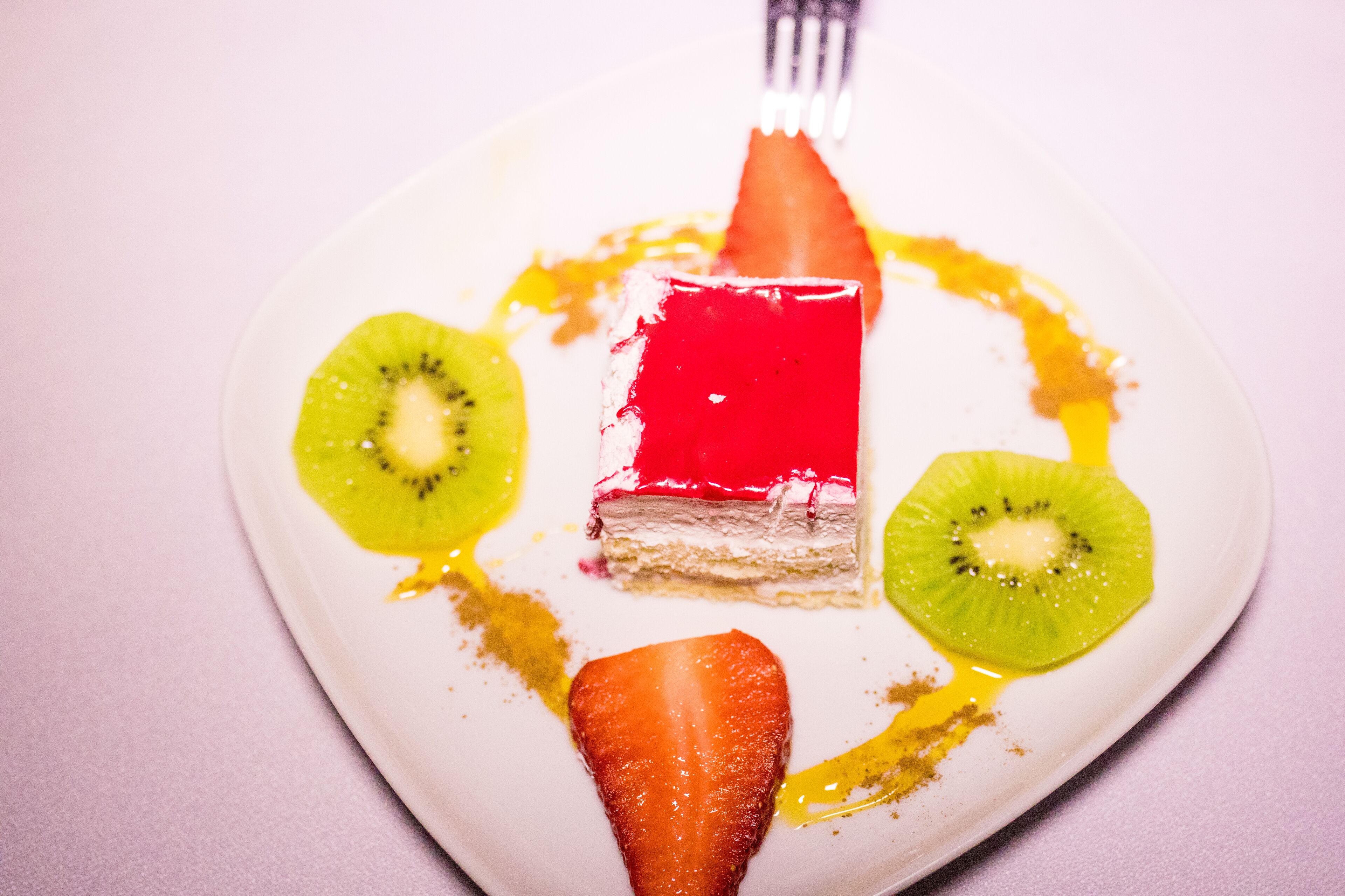 Un plato de postre con una porción de pastel de gelatina rojo, rodajas de kiwi y una fresa.
