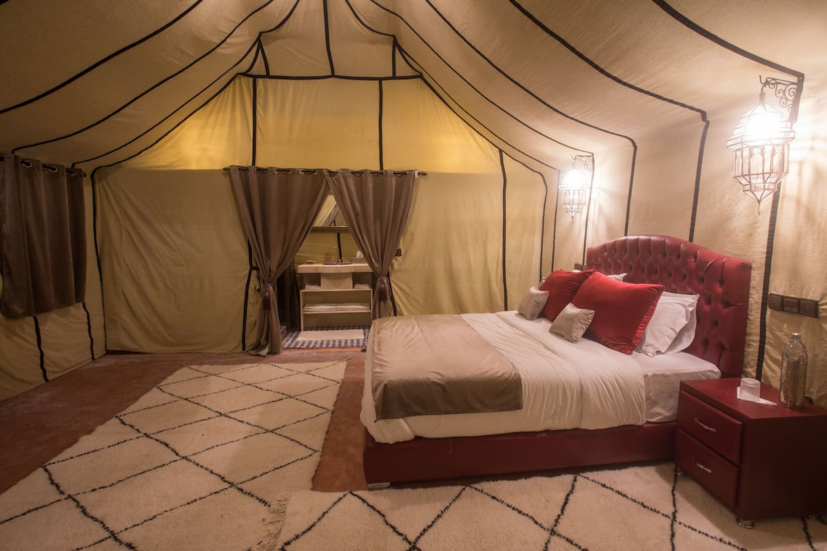 Um quarto com tenda, uma cama, uma mesa de cabeceira e um abajur.
