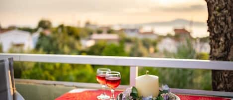 A balcony with a table set for two, featuring a candle, a plate of flowers, and two glasses of red wine.