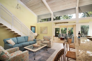 A spacious living area with a high ceiling, a staircase, and a view of the outdoors.