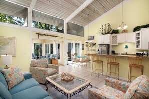 A spacious living area with a high ceiling, a dining area, and a kitchen with white cabinets.