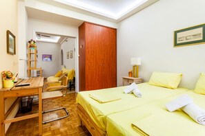 A hotel room with a bed, a desk, a chair, a wardrobe, and a small table with a lamp. - Zografou's Hidden Gem - Athens Charming Home (Zografou)