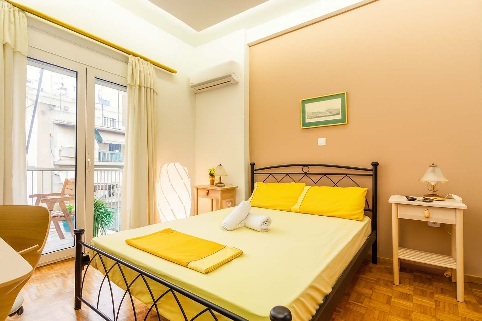 A neatly made bed with yellow bedding, a bedside lamp, and a small table with a lamp.