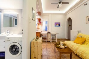 Een ruimtelijke woonkamer met een wasmachine, een eettafel, een bank en een plafondventilator.