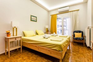 A hotel room with a wooden bed, a desk with a lamp, a chair with a cushion, and a window with curtains.