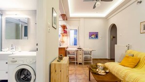 Ett kompakt bostadsutrymme med tvättmaskin, matplats, soffa och en takfläkt.