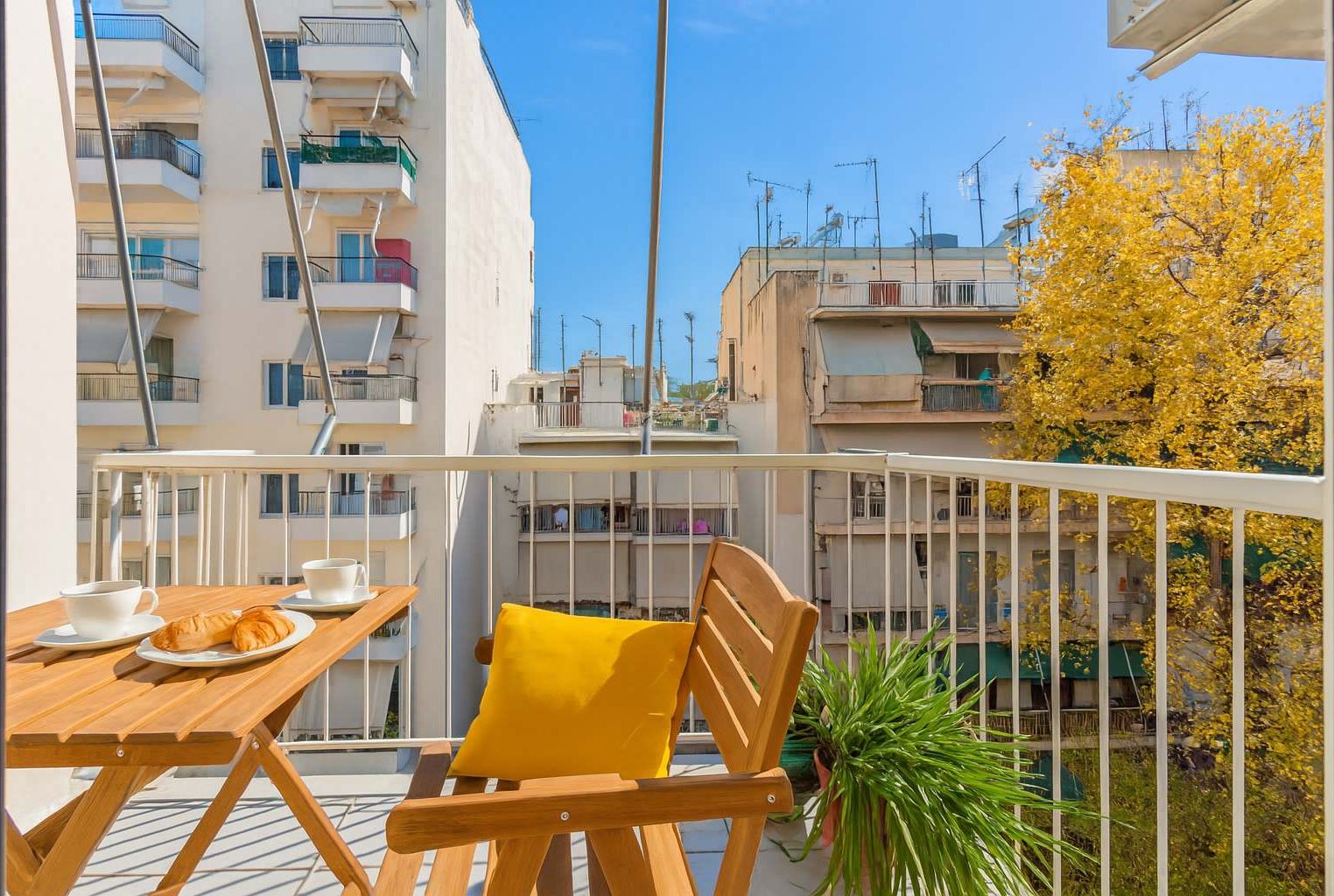 A balcony with a wooden table, two chairs, a yellow cushion, and a potted plant.