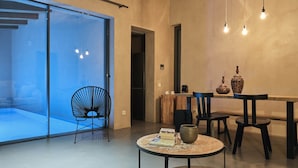 Un espace repas moderne avec une cloison en verre, une table ronde ornée de livres, une cafetière et deux vases.