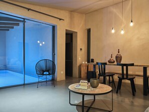 A modern dining area with a glass partition, a round table with books, a coffee pot, and two vases.