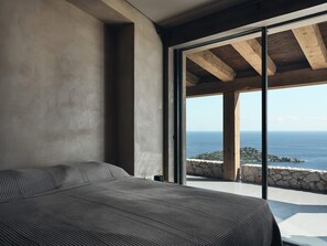 A bedroom with a large bed, a stone wall, and a view of the sea.
