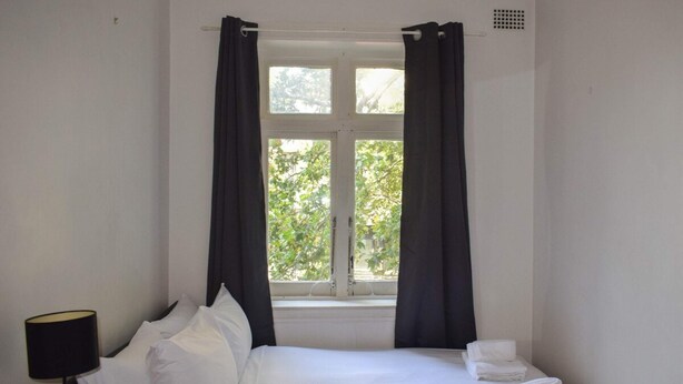 A hotel room with a bed, a nightstand with a lamp, and a window with curtains. - Incredible Location One Bedroom Apartment (Potts Point)