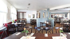 En restaurang med flera bord och stolar, en bardisk och ett kök som syns i bakgrunden.