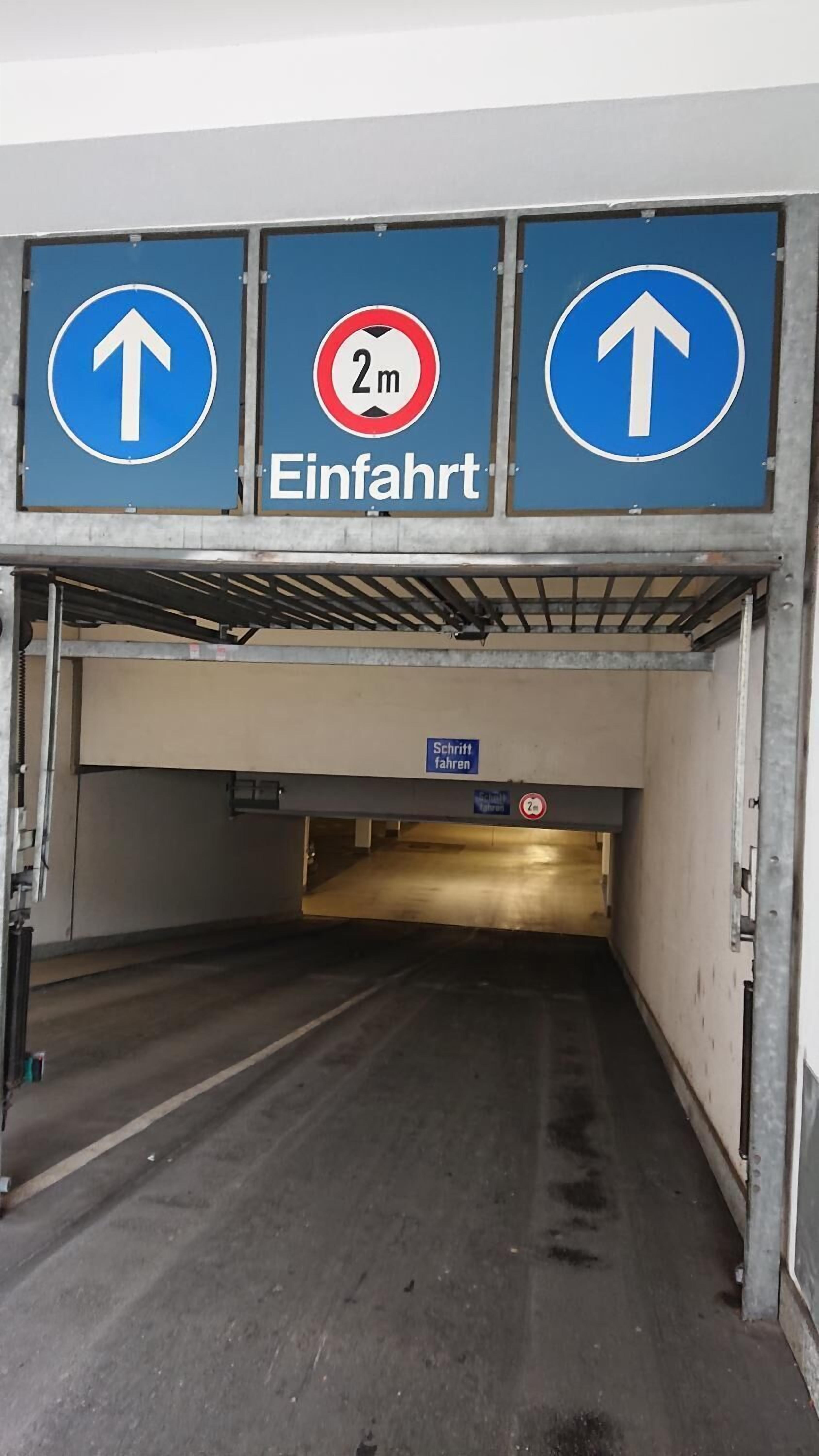A parking garage entrance with directional signs and a height restriction sign.