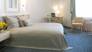 Ett hotellrum med en säng, ett skrivbord, en stol, en lampa och ett fönster med gardiner.