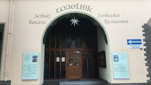 L’entrée d’un restaurant serbe, avec une porte en bois et une enseigne en plusieurs langues.