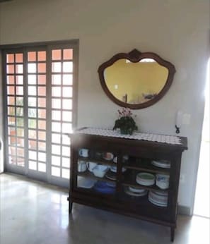 A room with a large window, a wooden cabinet with dishes, and a mirror on the wall. - Casa Relax Brotas (Brotas)