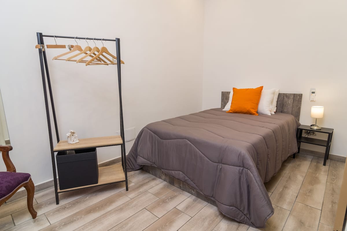 A bedroom with a bed, a nightstand, a bedside table, a wardrobe, and a chair.