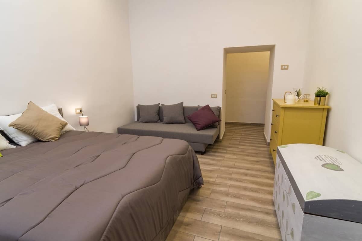 A bedroom with a bed, a sofa, a small cabinet, and a desk.