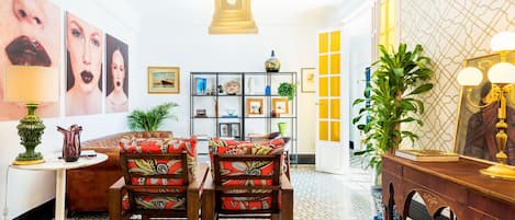 Una habitación con piso estampado, un sofá, dos sillas, una mesita, una estantería y un espejo con apliques de pared.