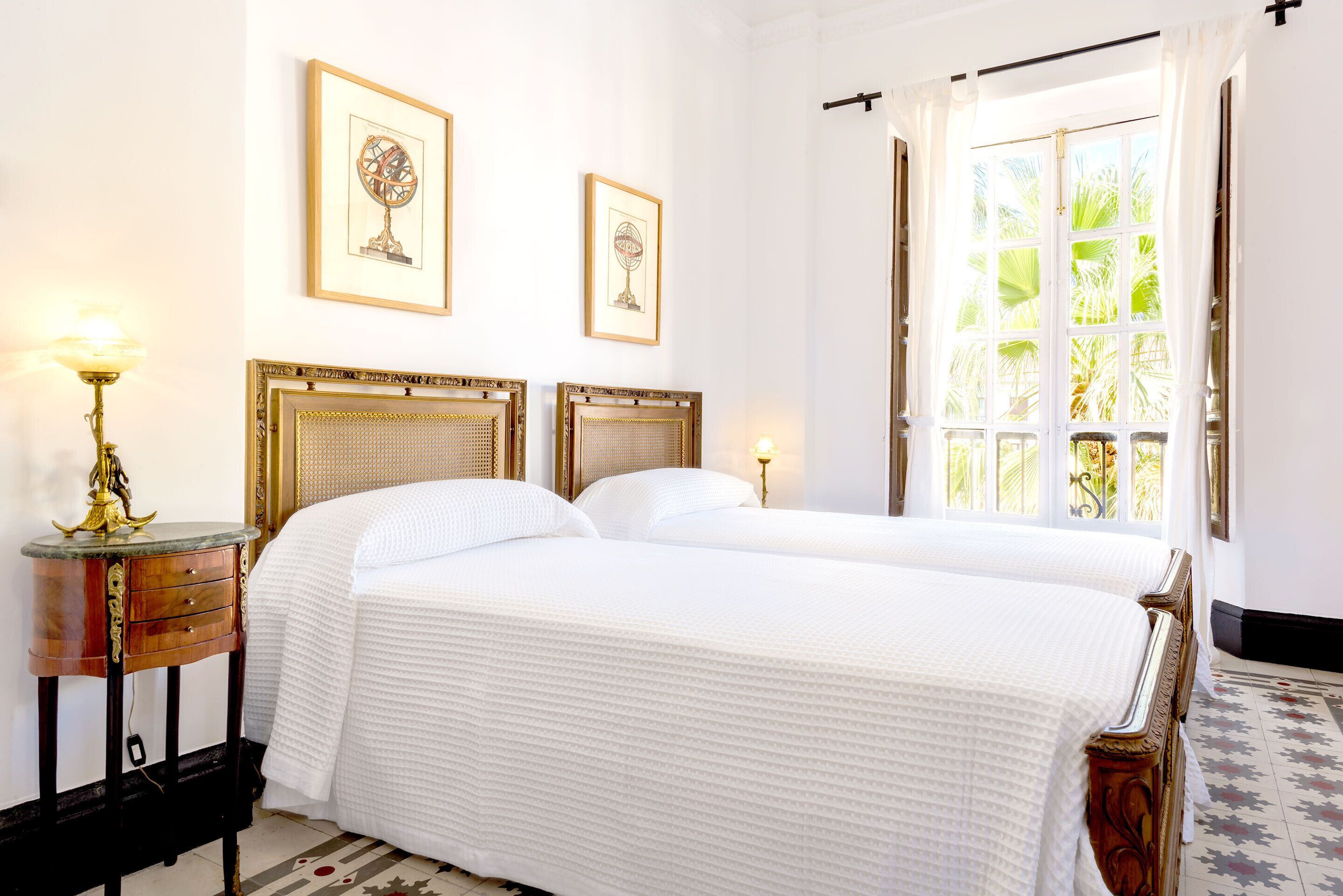 A hotel room with two beds, a window with curtains, and two framed pictures on the wall.