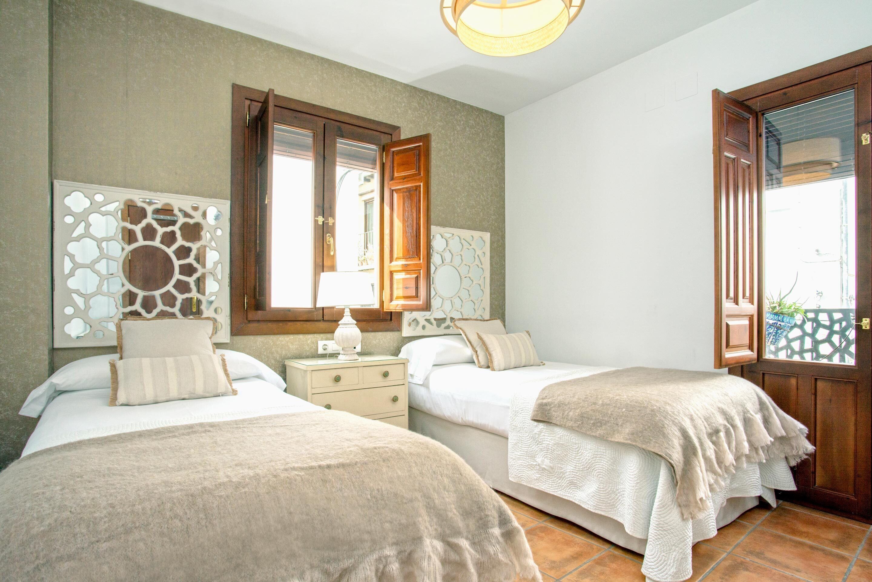 A bedroom with two beds, a nightstand, a decorative wall piece, and a wooden door.