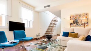 A modern living room with a glass coffee table, blue chairs, a white sofa, and a staircase. - Genteel Home Francos Terrace V (Seville)