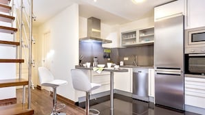 A modern kitchen with stainless steel appliances, a bar area with stools, and a wooden staircase. - Genteel Home Francos Terrace V (Seville)