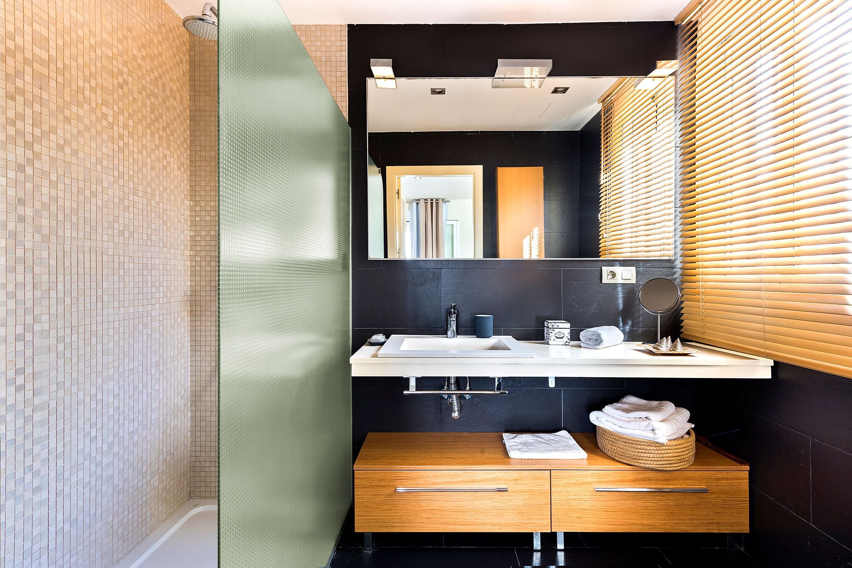 Ein modernes Badezimmer mit einer Glasdusche, einem Holzkosmetikschrank mit Waschbecken und einem Spiegel darüber.