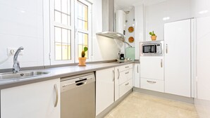 A modern kitchen with white cabinets, a dishwasher, a microwave, and a window with blinds. - Genteel Home Vinuesa (Seville)