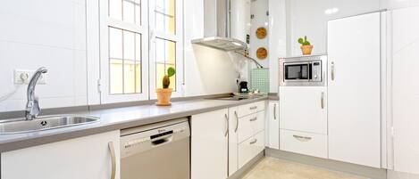 A modern kitchen with white cabinets, a dishwasher, a microwave, and a window with blinds.
