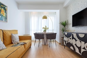 Una sala de estar moderna con un sofá, una mesa de comedor, sillas, un televisor y un aparador decorativo.