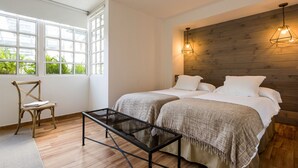 Une chambre avec deux lits, une tête de lit en bois, une fenêtre donnant sur un beau paysage et une petite table.