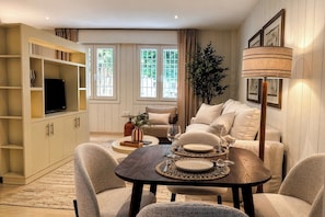 A modern living room with a sofa, a dining table set for two, a TV on a cabinet, and a large plant. - Genteel Home San Leandro (Seville)