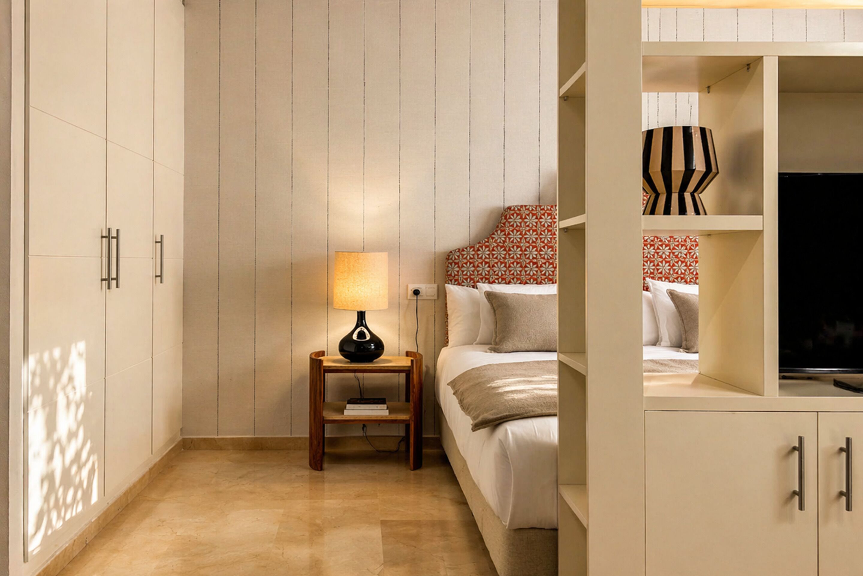 A bedroom with a bed, bedside table, lamp, and wardrobe.