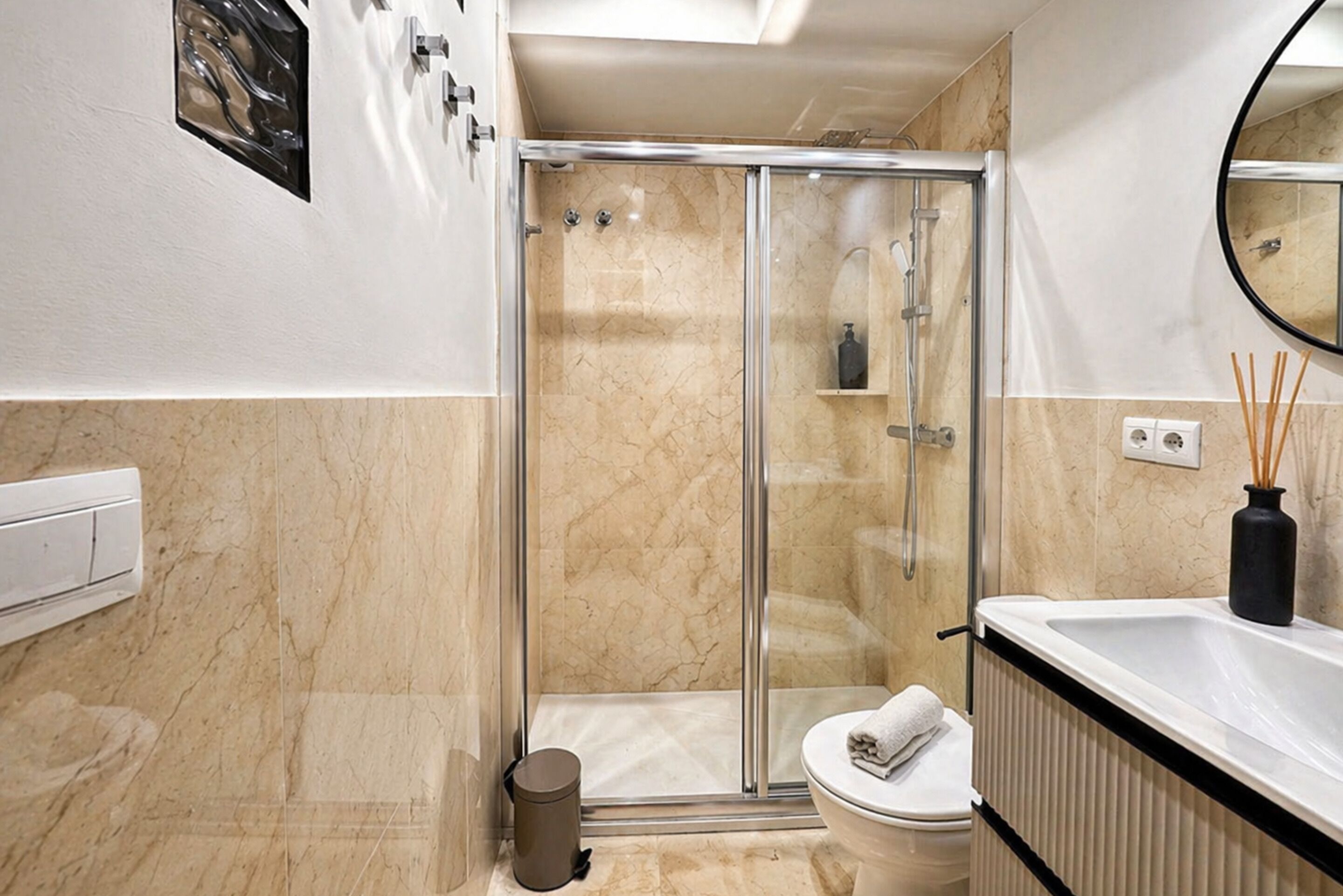 Une salle de bain moderne avec une douche à parois de verre, des toilettes blanches et un lavabo noir.