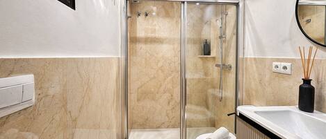 Une salle de bain moderne avec une douche à parois de verre, des toilettes blanches et un lavabo noir.