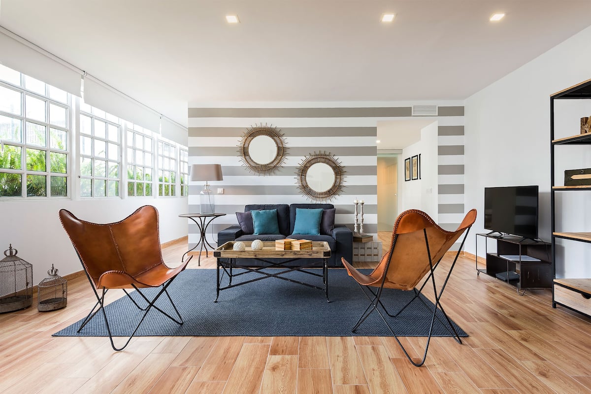 Una sala de estar moderna con un sofá, dos sillones de cuero, una mesita de centro y un televisor.