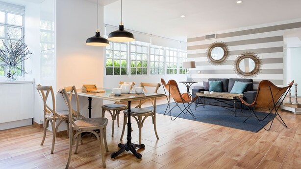 Un vaste espace dédié à la salle à manger, avec une table et des chaises en bois, un canapé agrémenté de coussins et une grande fenêtre laissant entrer la lumière naturelle.