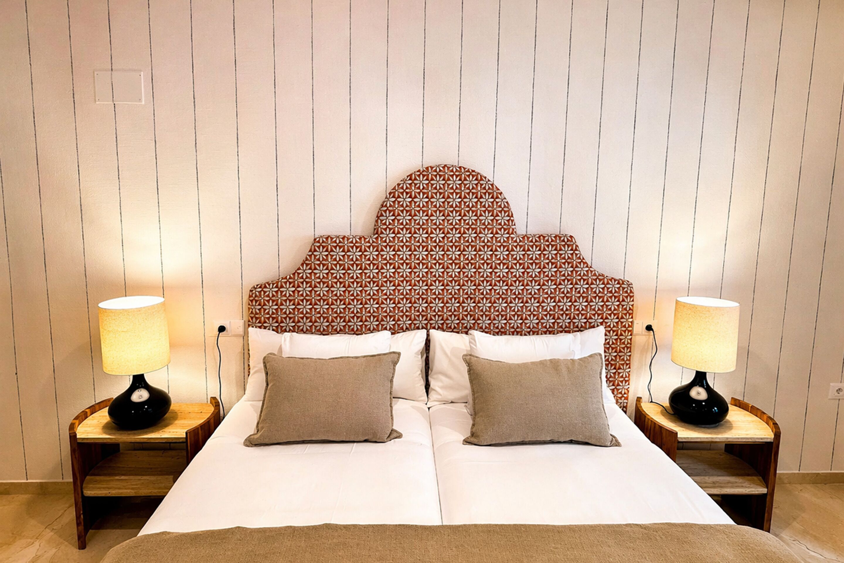 Una cama doble con cabecera estampada, dos lámparas de noche y dos almohadas.