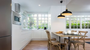 Une cuisine moderne avec des meubles blancs, un réfrigérateur en acier inoxydable, un four à micro-ondes et un coin repas comprenant une table et des chaises en bois.