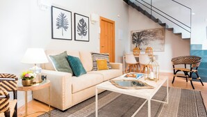 A modern living room with a sofa, coffee table, and chairs, a staircase, and artwork on the walls.