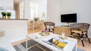 A modern living room with a sofa, coffee table, and two patterned chairs. A dining area with a table and chairs is visible in the background. - Genteel Home Trinidad Grund G (Málaga)
