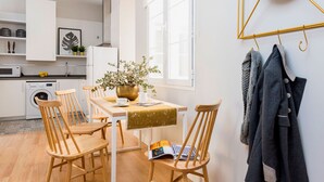 A modern kitchen with a dining area, wooden chairs, a table with a gold table runner, and a hanging coat rack. - Genteel Home Trinidad Grund G (Málaga)