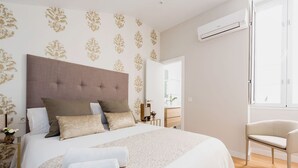 A bedroom with a large bed, a bedside table, a chair, and an air conditioning unit. - Genteel Home Trinidad Grund G (Málaga)
