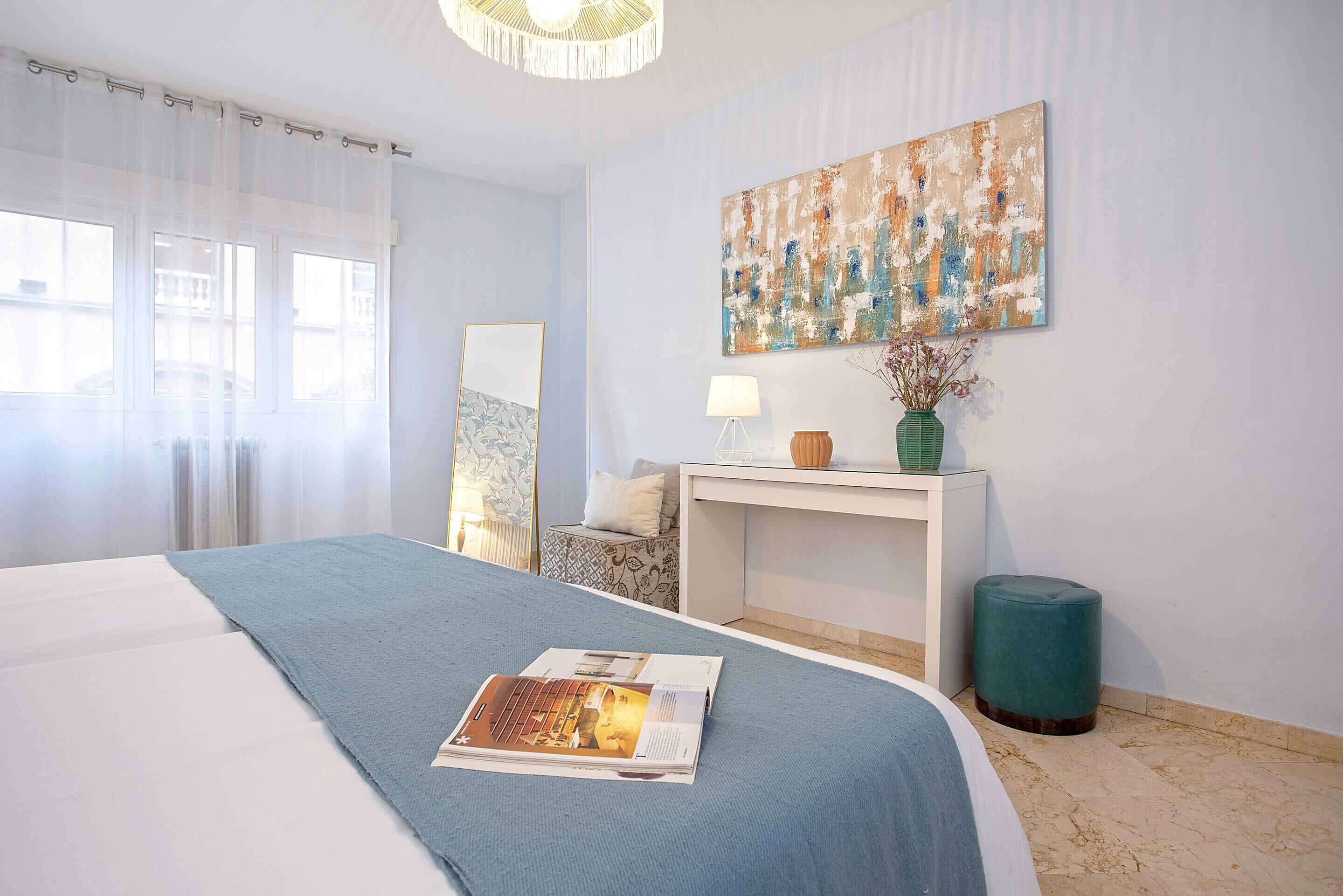 A bedroom with a bed, a desk, a chair, a lamp, and a painting on the wall.