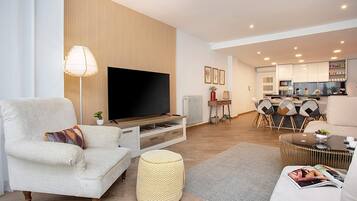 Una sala de estar moderna con un televisor de pantalla plana, un sofá, una mesa de centro y una zona de comedor con sillas y una mesa pequeña.